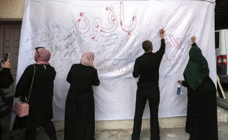 A color photograph from on May 22, 2023, of displaced Palestinians in Gaza writing the names of the villages from which they were expelled during a commemoration of the 75th anniversary of the Nakba on a large white sheet