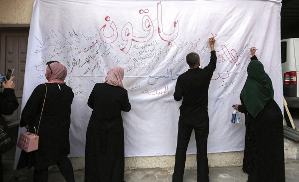 A color photograph from on May 22, 2023, of displaced Palestinians in Gaza writing the names of the villages from which they were expelled during a commemoration of the 75th anniversary of the Nakba on a large white sheet