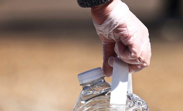 Photo of a gloved hand holding a gallon bottle of water.