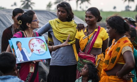 Maya Patil holds open a book depicting the uterus to a group of migrant sugarcane workers in India.