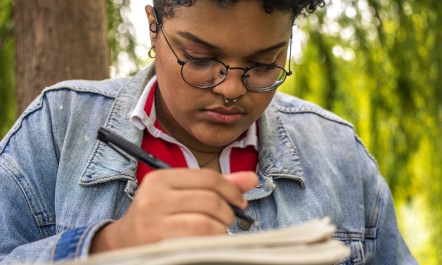 A photo showing afro-american woman writing notes in the woods.