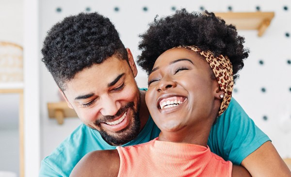 Photo of a Black woman and Black man embracing and smiling in their kitchen.